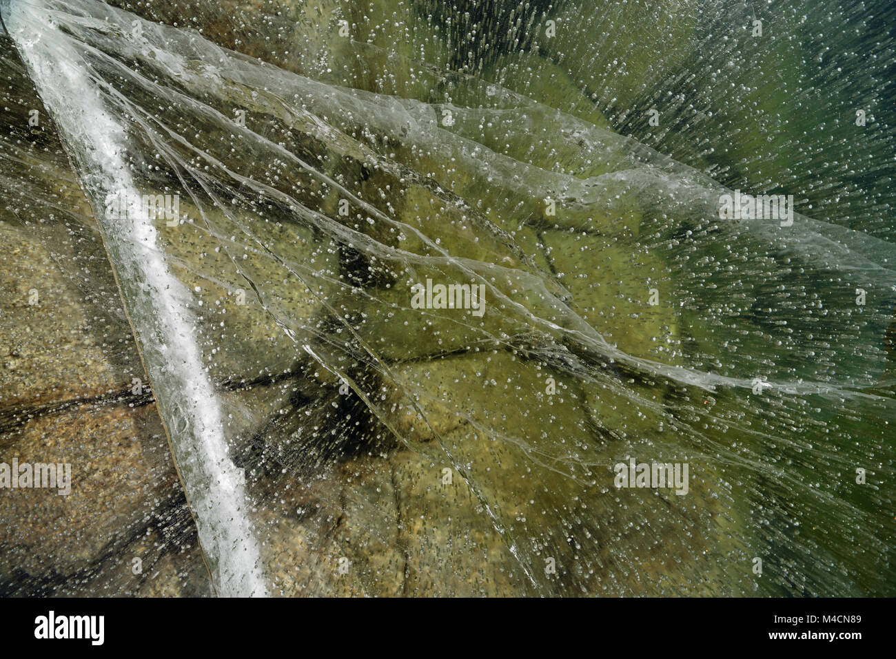 Ausblick in Risse im Eis auf einem zugefrorenen Bergsee mit Felsen auf der Unterseite Stockfoto