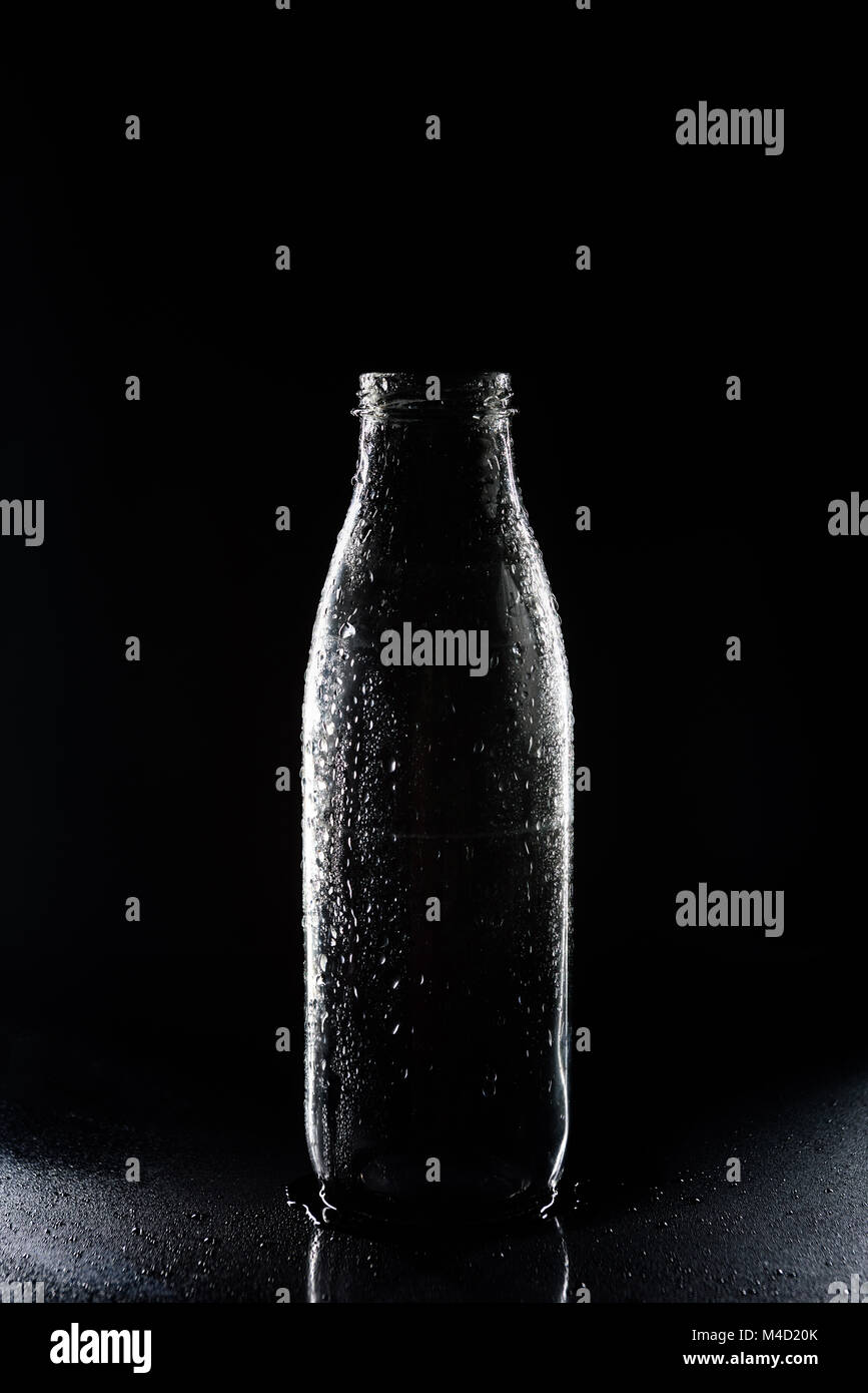 Eine transparente leere Glasflasche mit Kondensat auf Schwarz Stockfoto