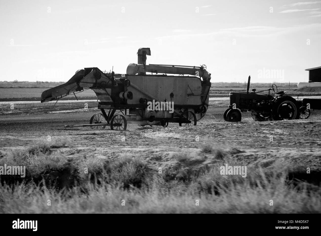 Eine altmodische Erntemaschine neben einem alten Traktor in Schwarz und Weiß. Stockfoto