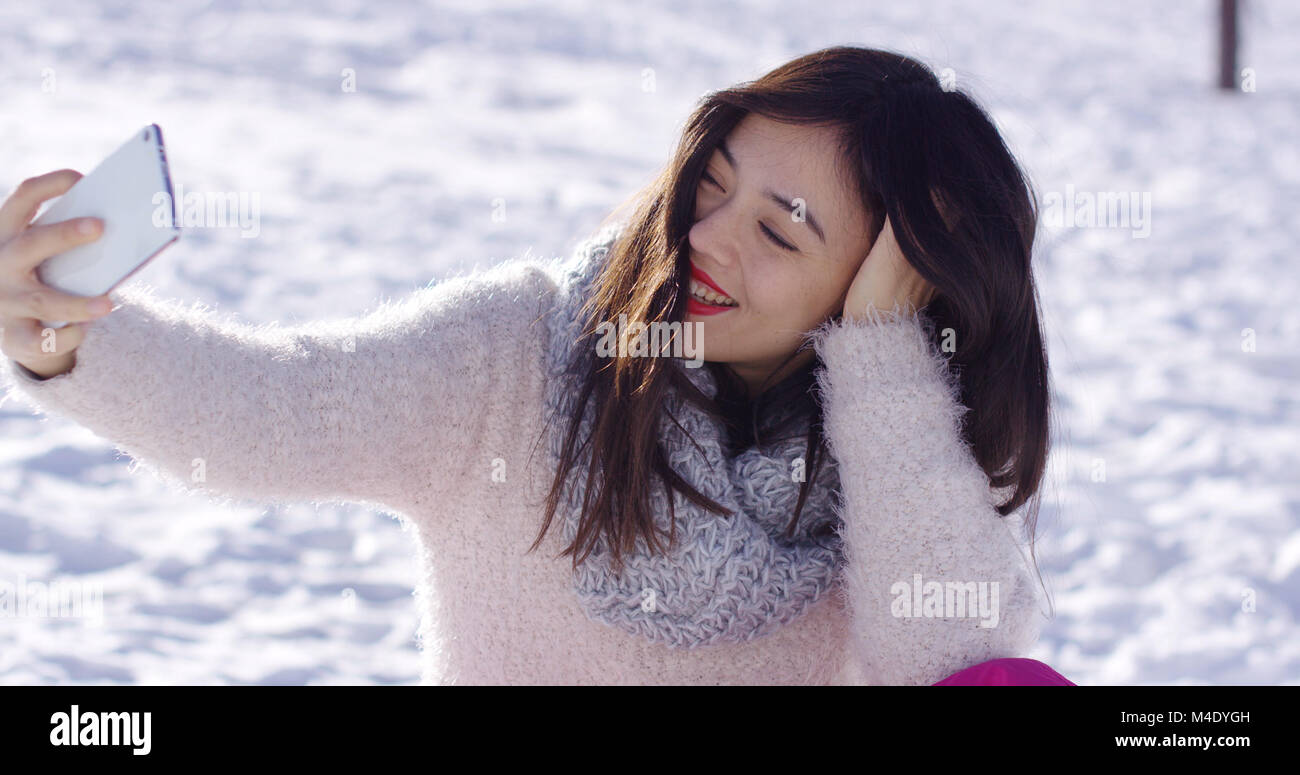 Hübsche Frau saß auf Schnee unter selfie Stockfoto