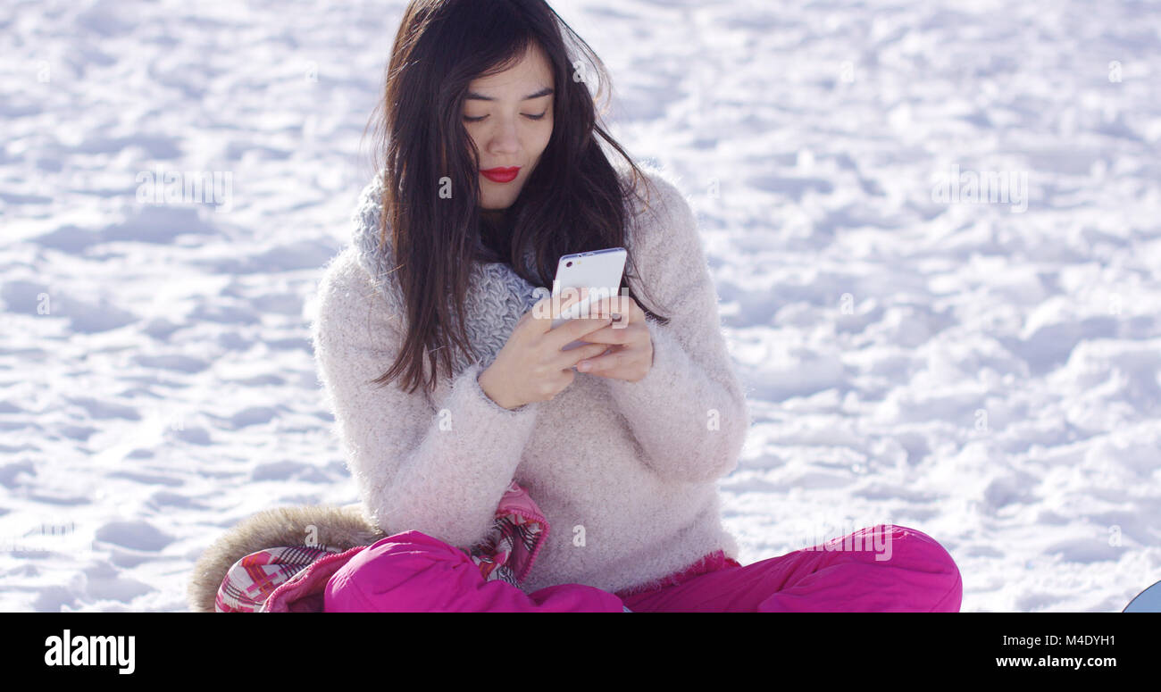 Junge Frau saß auf Schnee sms auf Mobile Stockfoto