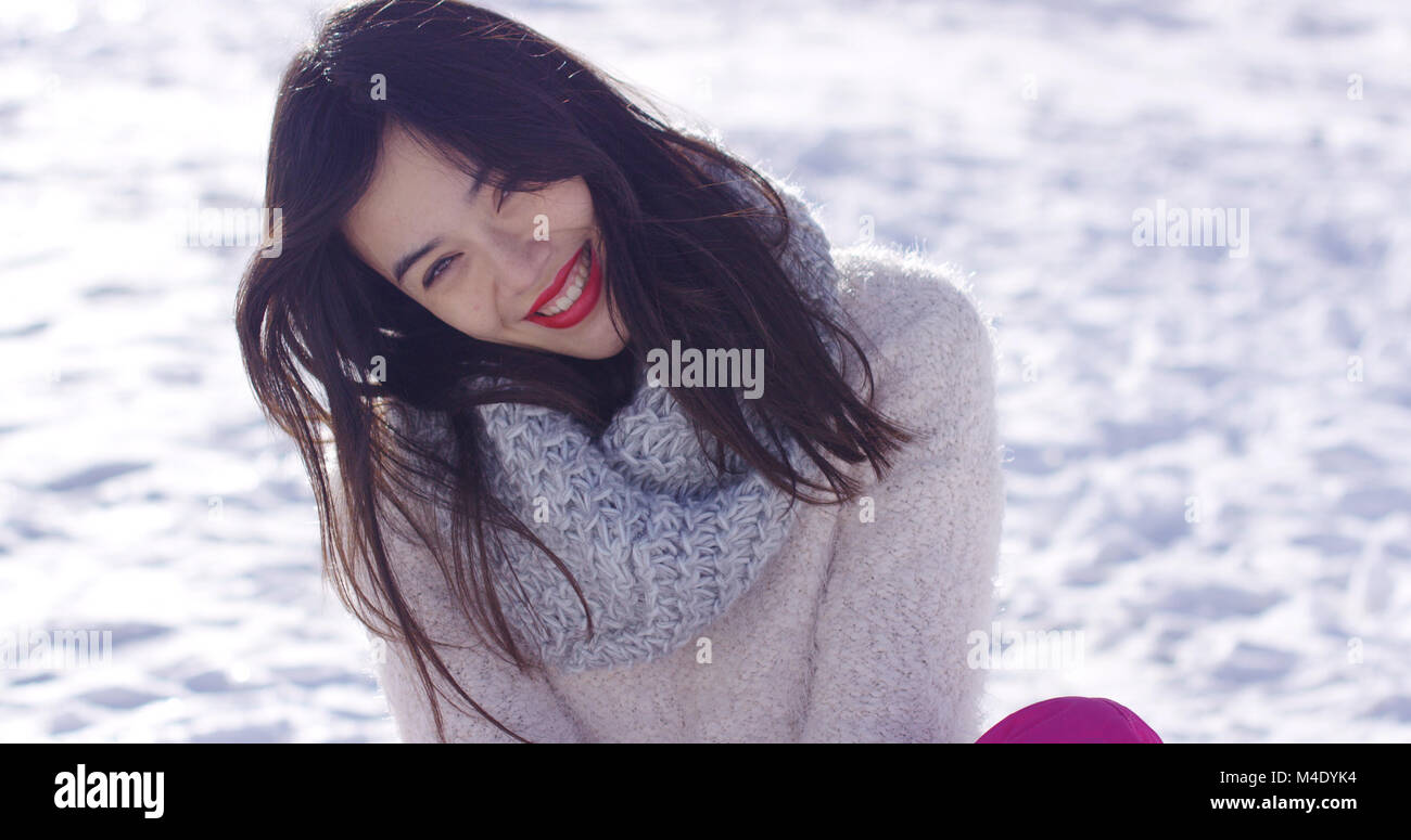 Lächelnde junge Frau saß auf Schnee Stockfoto