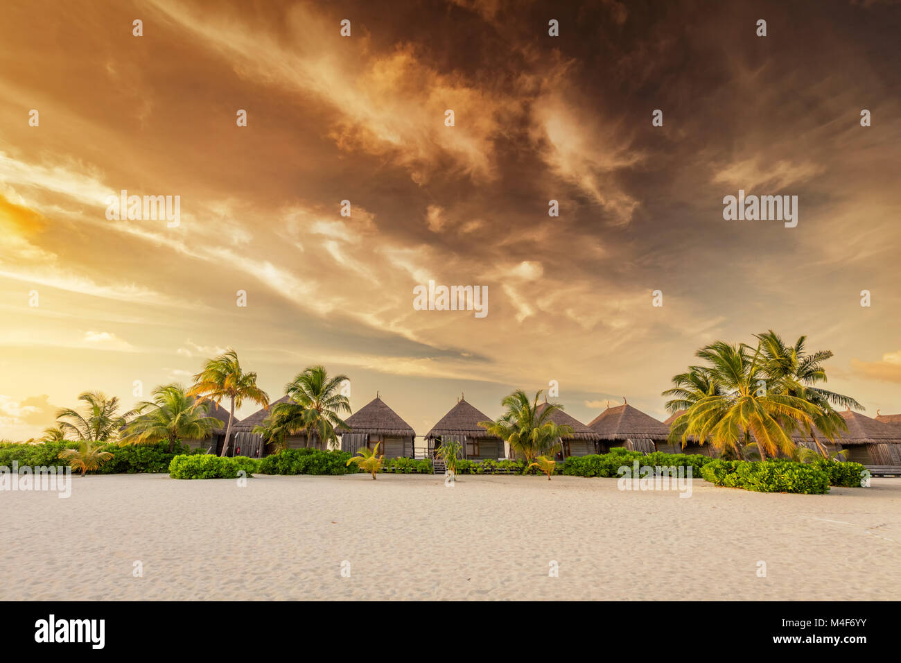 Strand und Villen auf einer Insel auf den Malediven bei Sonnenuntergang Stockfoto