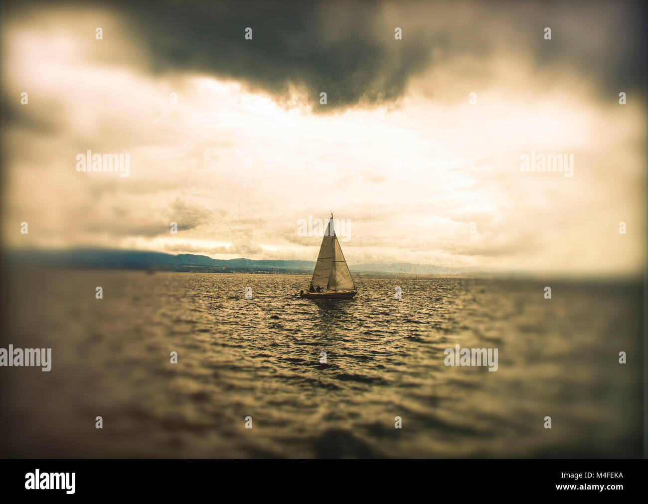 Segeln auf einem ruhigen Meer unter einem stimmungsvollen Himmel mit einem einsamen Segelboot in der Ferne am frühen Abend, dem Genfer See. Schweiz Stockfoto