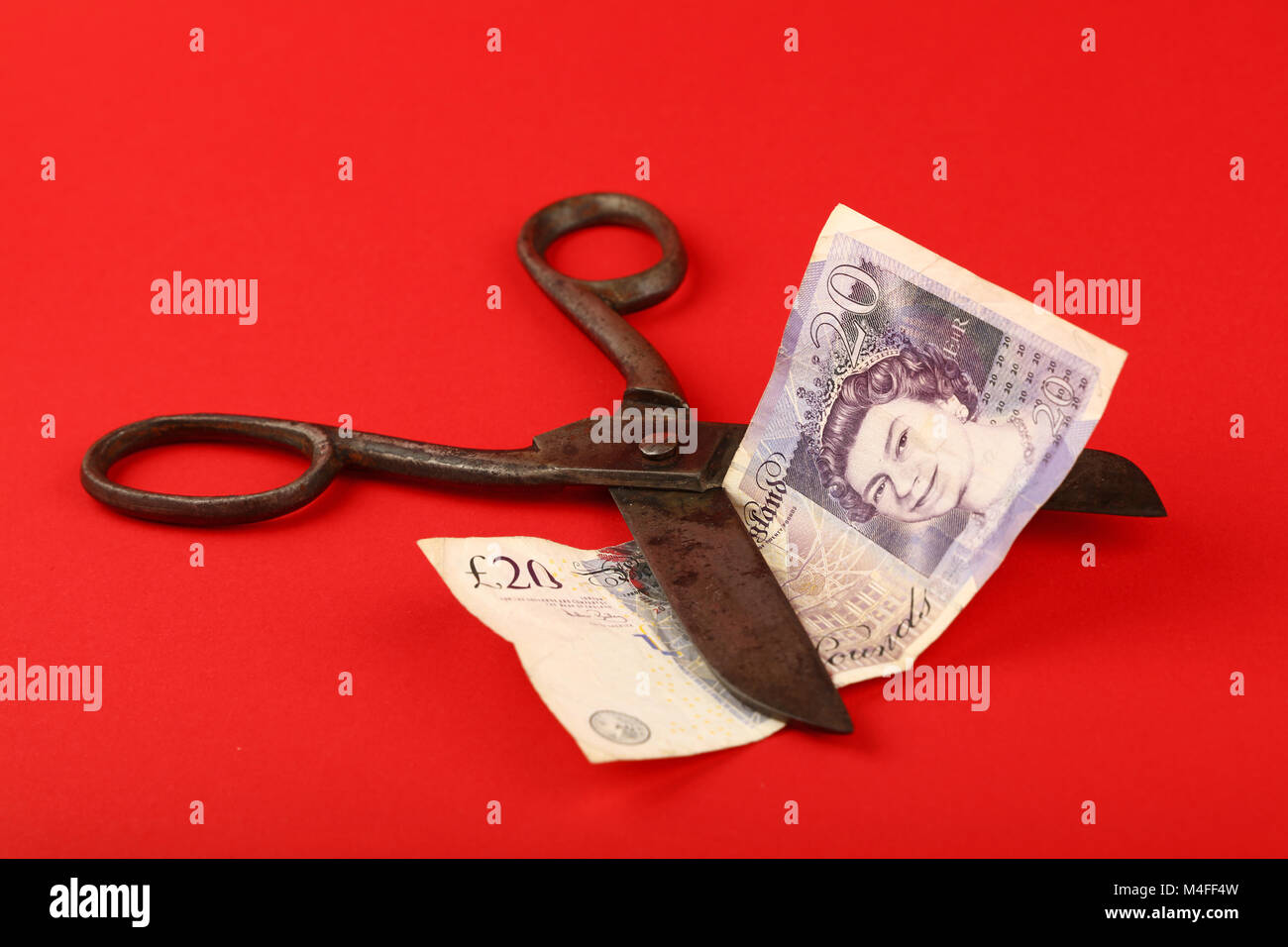 UK und Großbritannien Finanzkrise Niedergang der britischen Wirtschaft und Pfund illustrierte, alte Vintage Schere schneiden zwanzig Pfund Banknote über rot Stockfoto