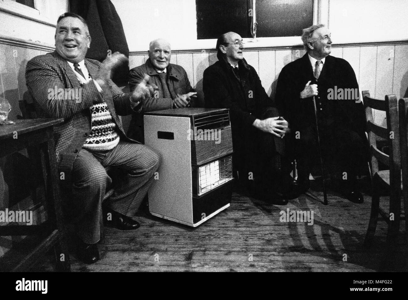 Vier alte Männer drängten sich um Gas Feuer Darsteller auf kleine Eisteddfod in Village Hall an Abergorlech Dyfed Wales UK hören Stockfoto