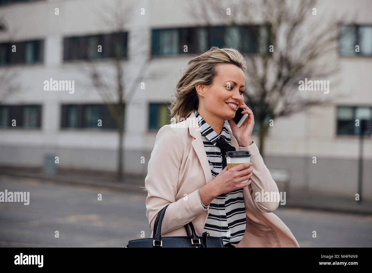 Geschäftsfrau ist zu Fuß in der Stadt zu arbeiten. Sie hält eine Kaffeetasse und ist, am Telefon zu sprechen. Stockfoto