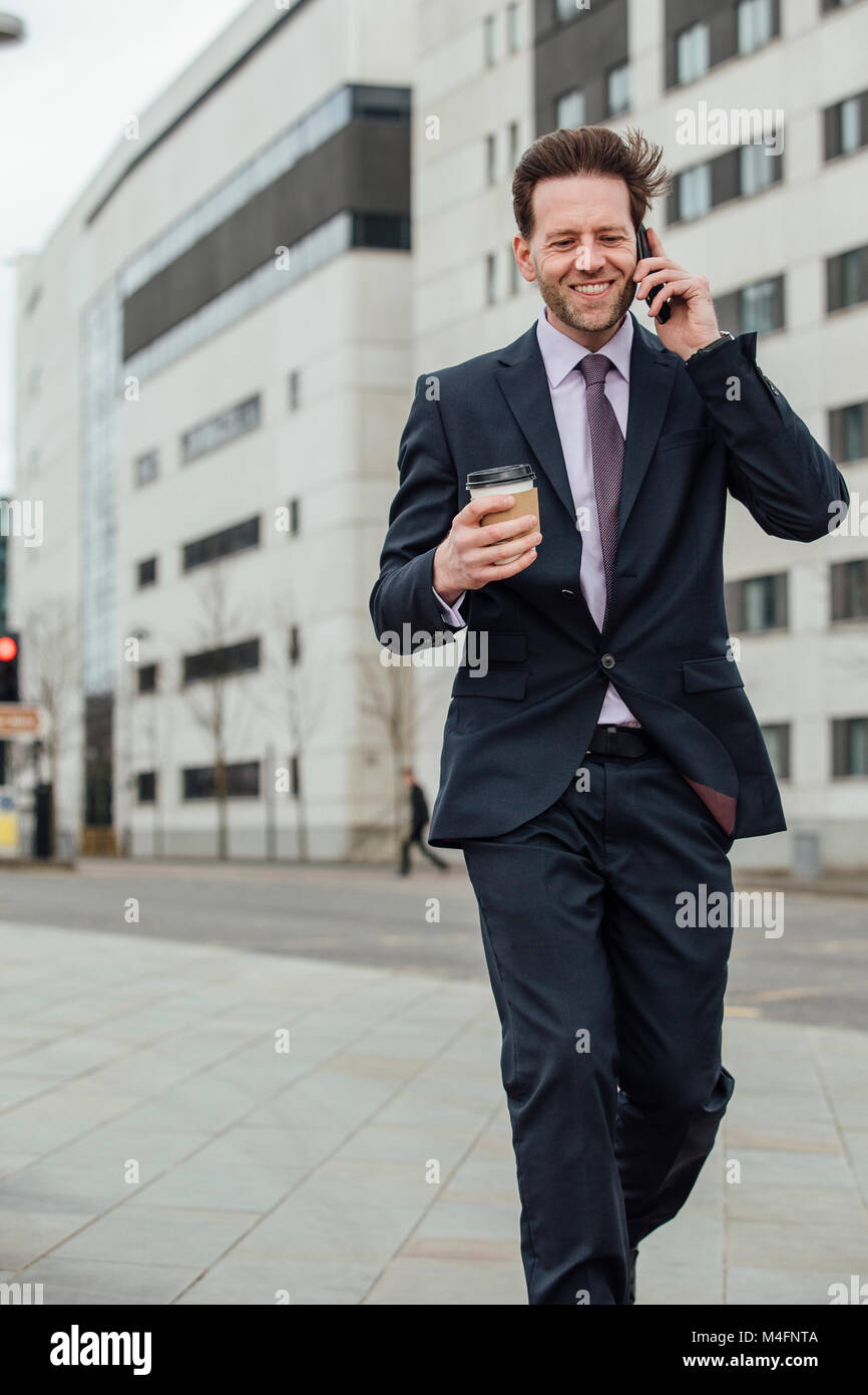 Unternehmer ist zu Fuß in der Stadt zu arbeiten. Er hält eine Tasse und ist, am Telefon zu sprechen. Stockfoto