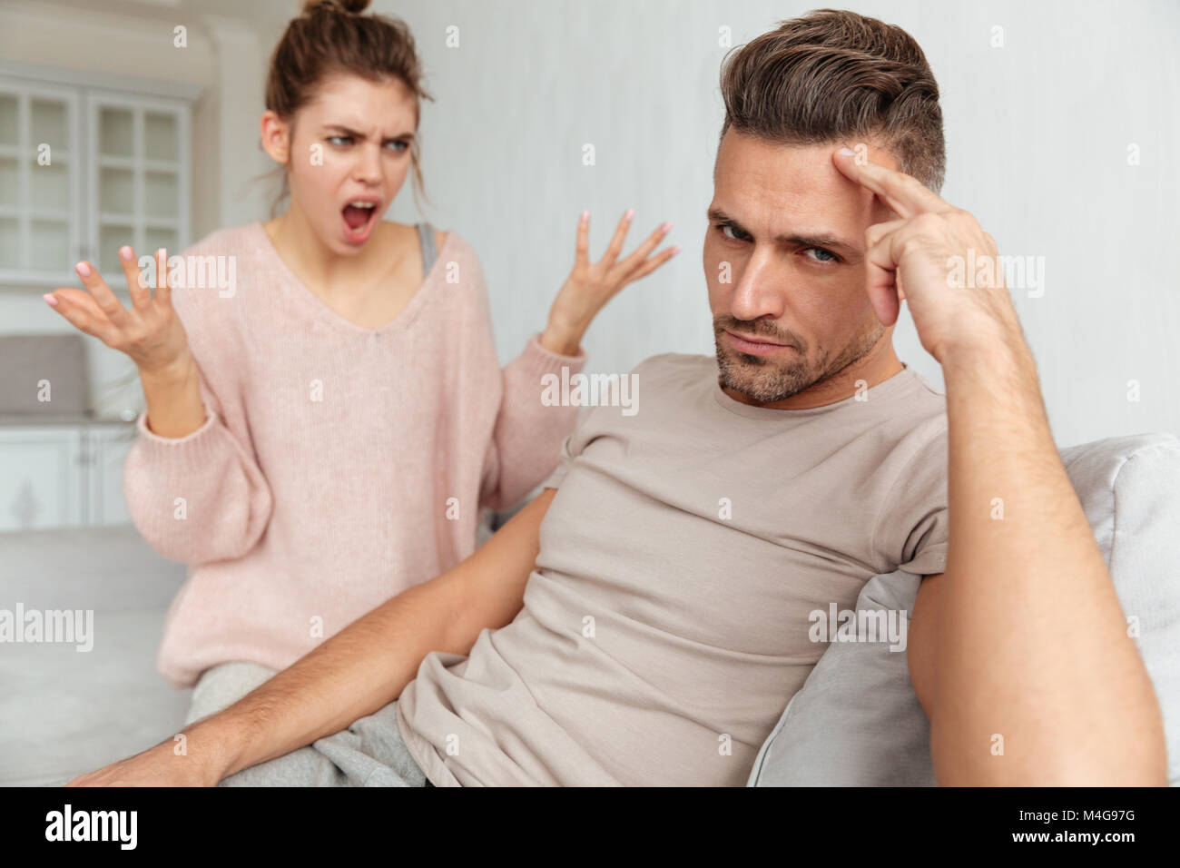 Unzufriedene Menschen auf der Couch mit seiner Freundin, die schreien und Streitereien mit ihm zu Hause sitzen Stockfoto