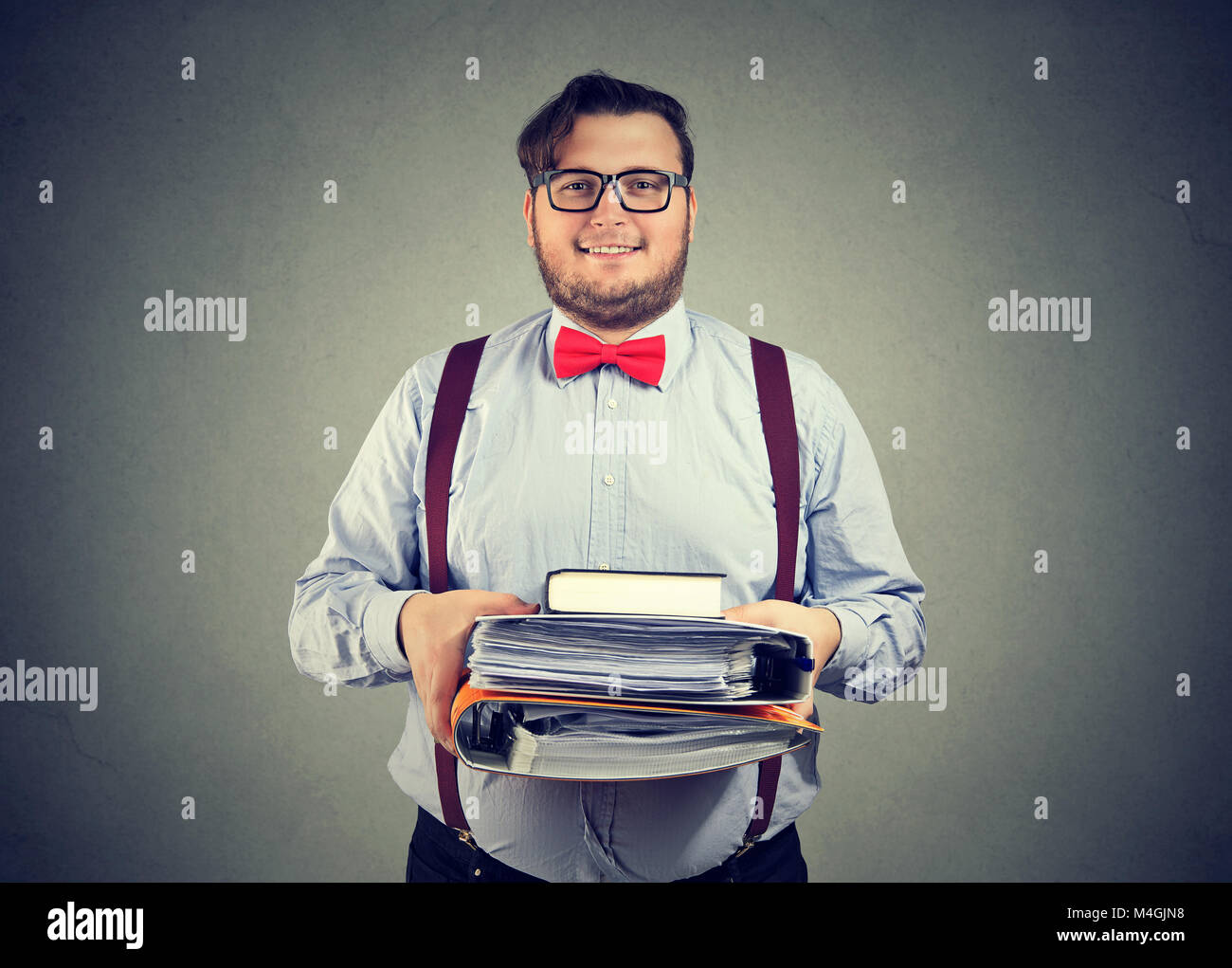 Intelligenter Mann in Brillen holding Stapel Bücher und Papiere suchen zufrieden an der Kamera. Stockfoto