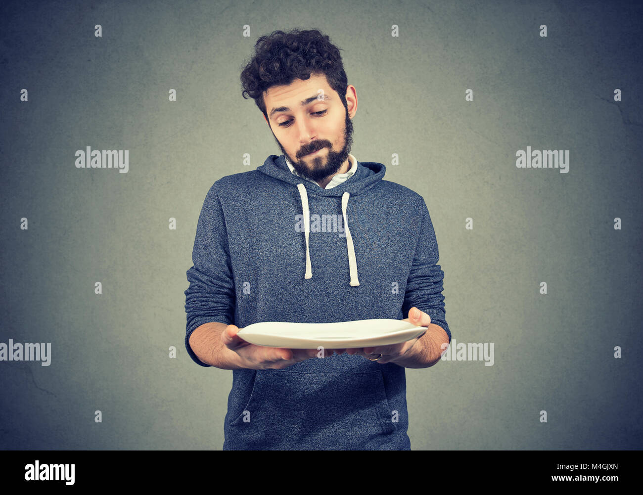 Junge bärtige Mann an leeren Teller in Dilemma mit Diät Wahl suchen. Stockfoto