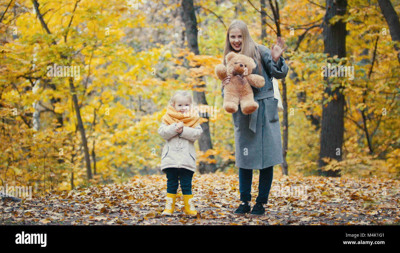Hübsche kleine Tochter mit ihrer Mama spielt mit gelben Blätter im Herbst Park Stockfoto