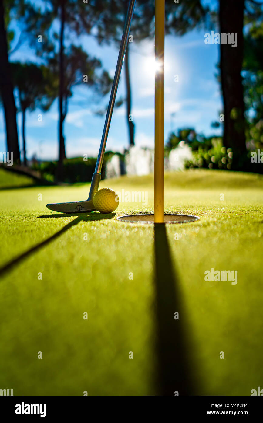 Minigolf gelben Ball mit einem Schläger in der Nähe der Bohrung bei Sonnenuntergang Stockfoto