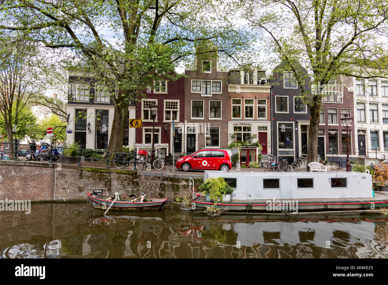 Amsterdam Canal mit Hausboot und Apartments auf der Straße hinter sich. Stockfoto