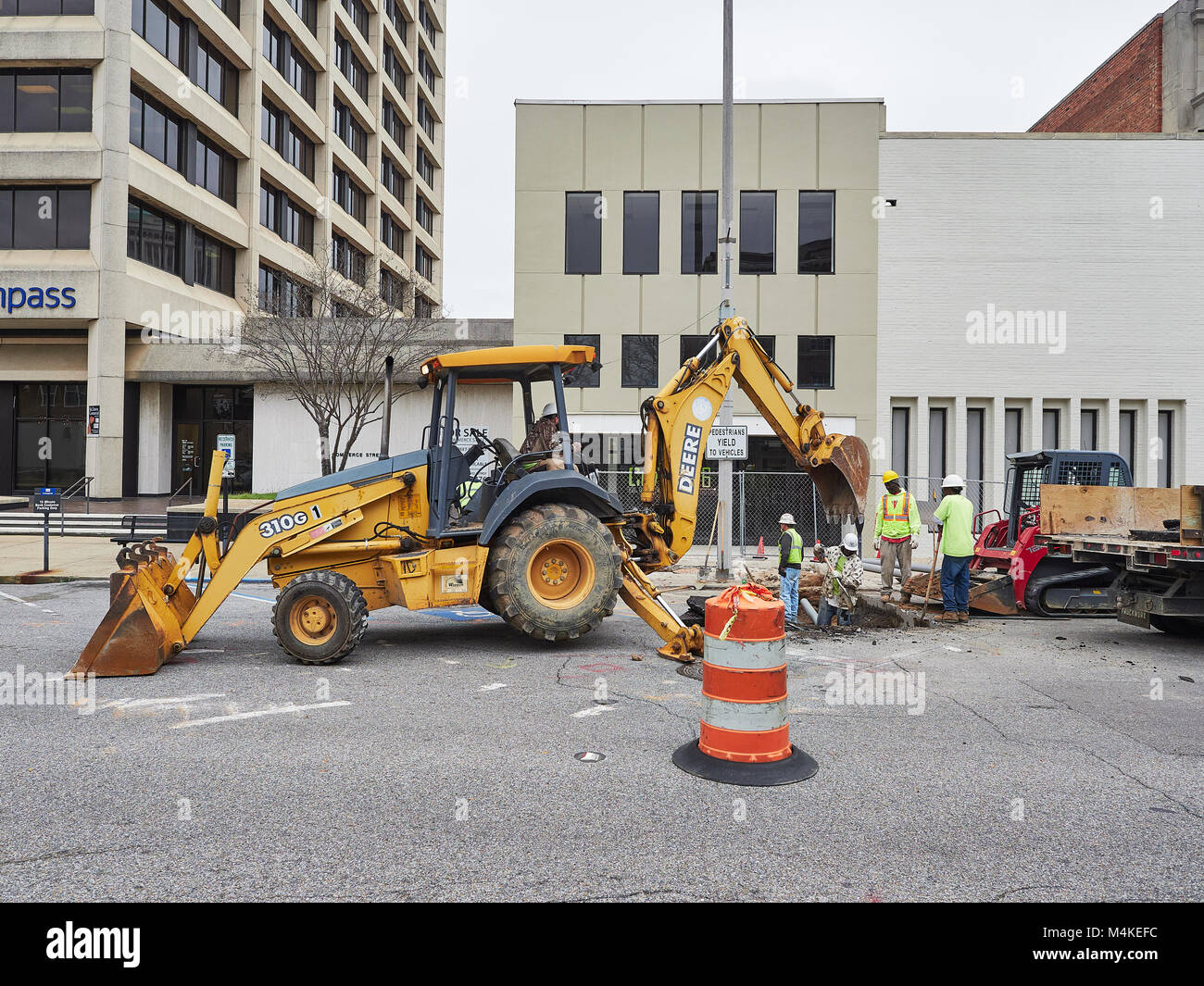 Bauarbeiten unter eine gepflasterte Straße der Stadt getan mit einer Hacke Frontlader und mehrere Arbeitnehmer in Montgomery Alabama, USA. Stockfoto
