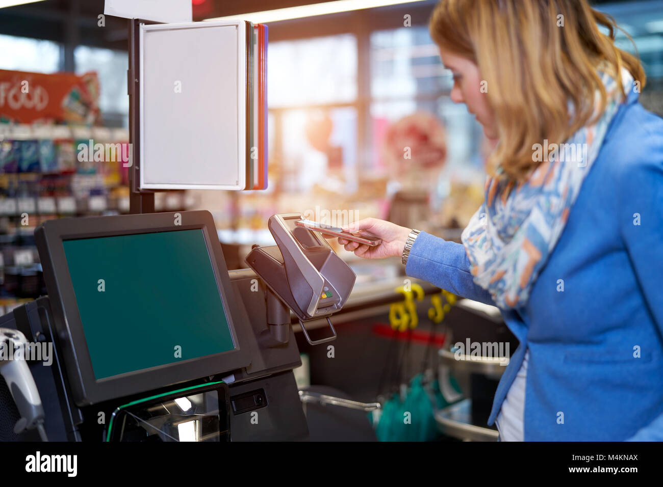 Junge Frau, die selbst-Kasse im Supermarkt mit Handy Stockfoto
