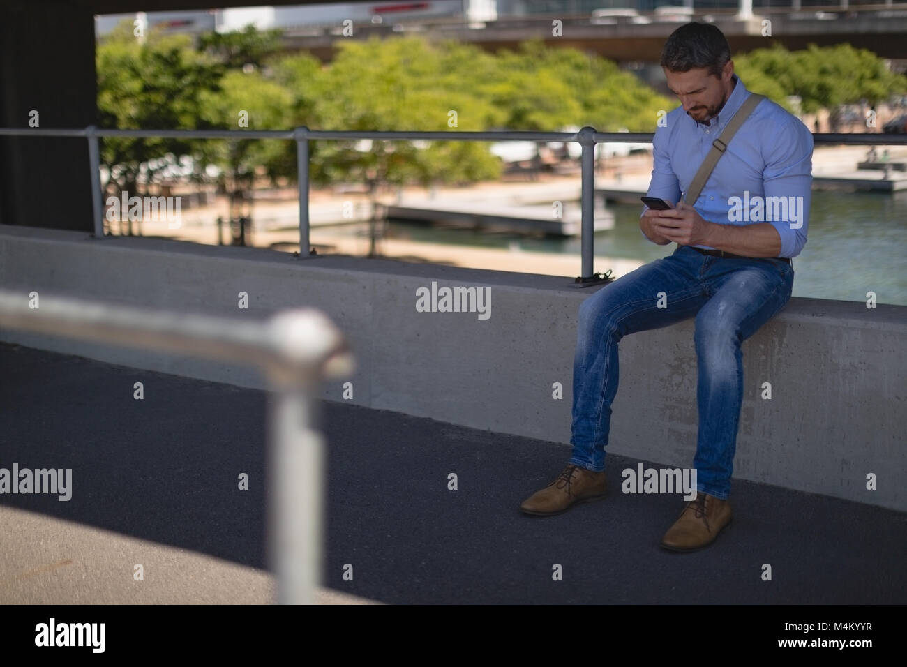 Mit Handy beim Sitzen auf Zaun Mann Stockfoto