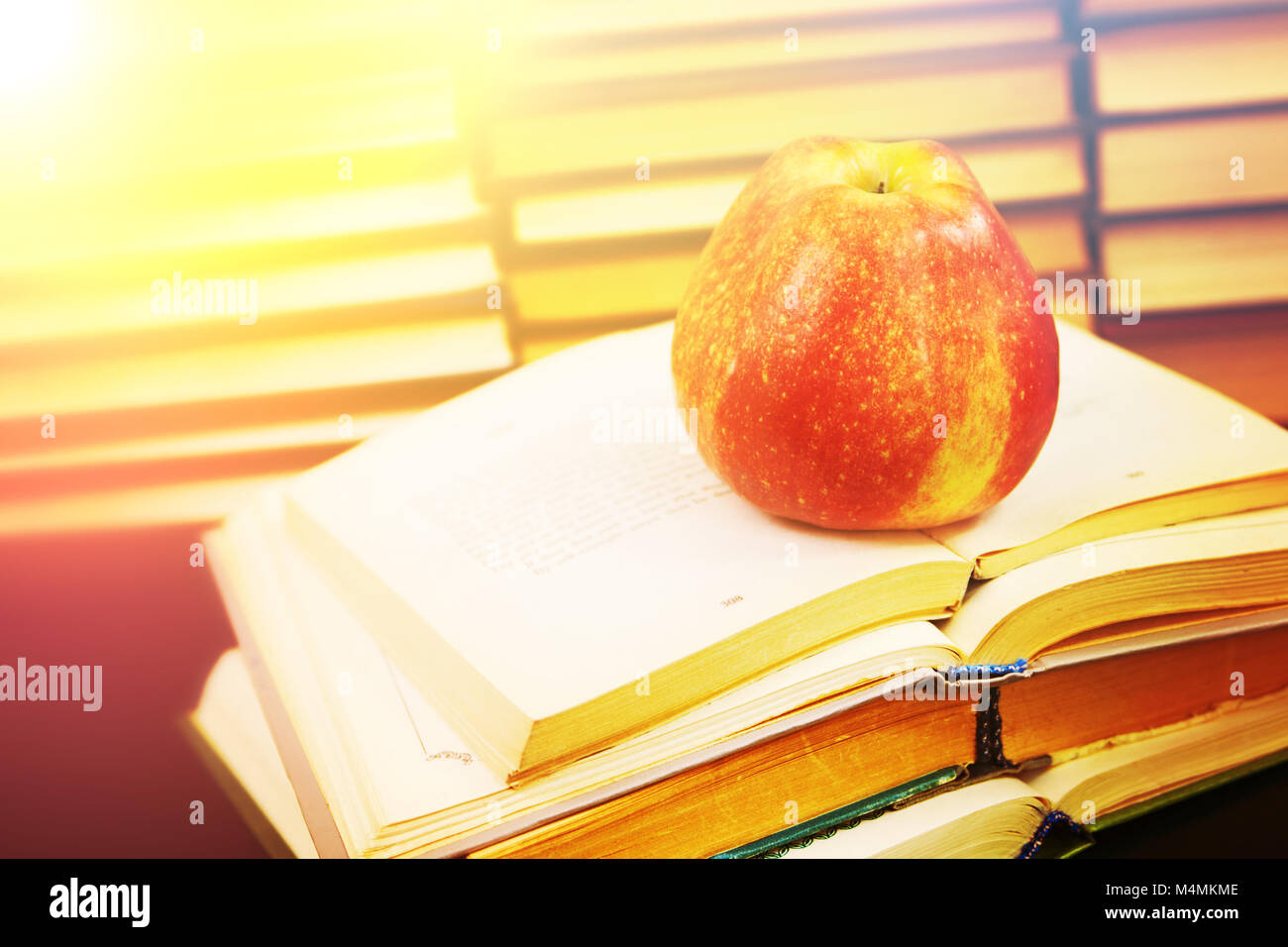 Roter Apfel auf das geöffnete Buch vor dem Hintergrund Stapel Bücher Stockfoto
