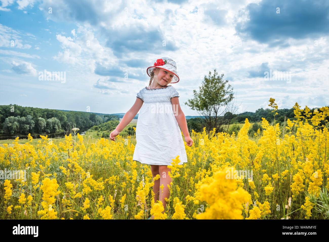 Süße kleine lachende Mädchen gehen in den Bereich der gelben Blumen Stockfoto