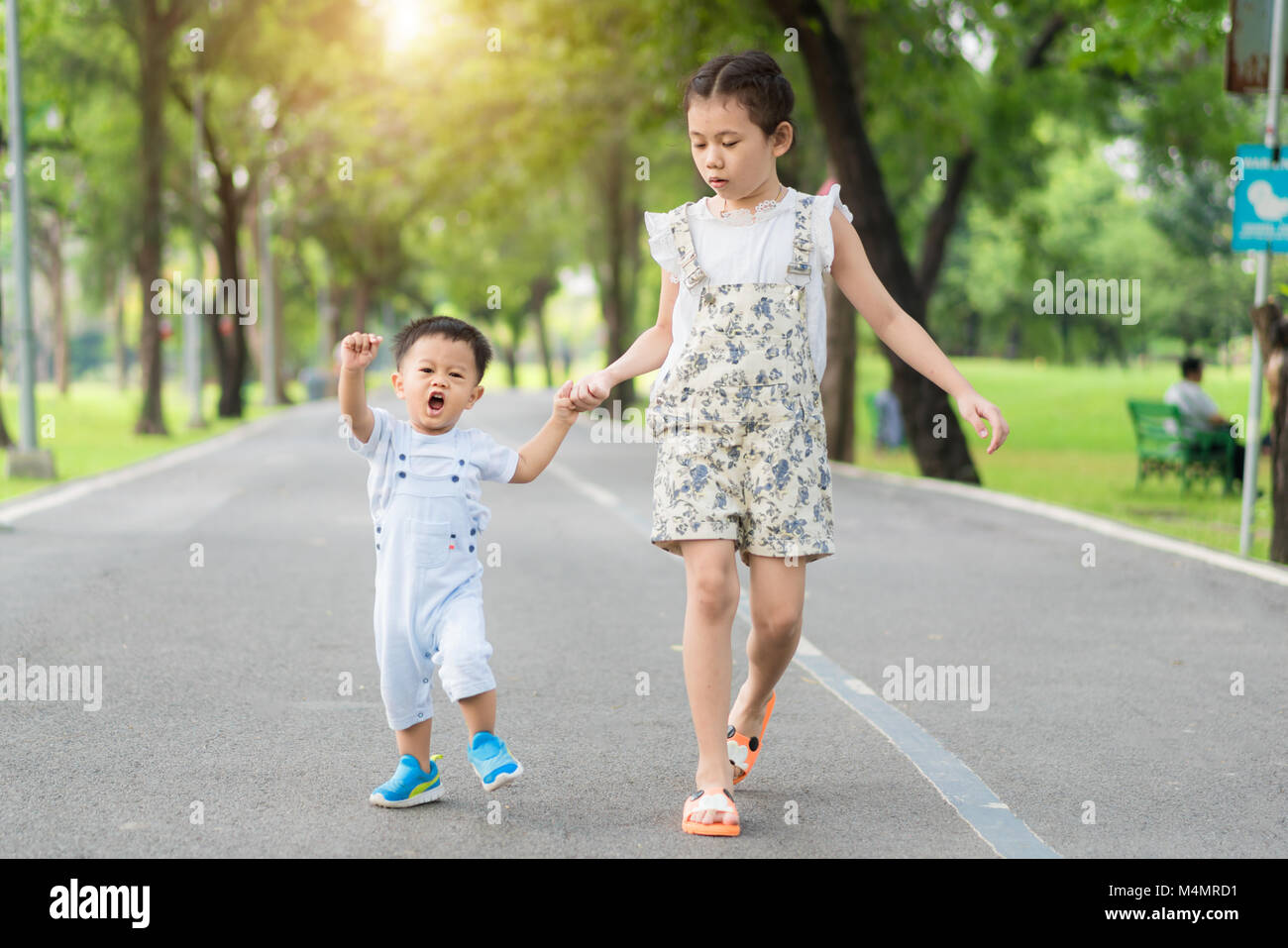 Asiatische Schwester halten Hände mit kleinen Kindern zu Fuß auf der Straße, im Park mit Sonnenstrahlen. Stockfoto
