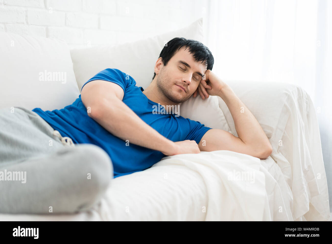 Zeit sich zu entspannen. Hübscher junger Mann schläft auf dem weißen Sofa zu Hause. Stockfoto
