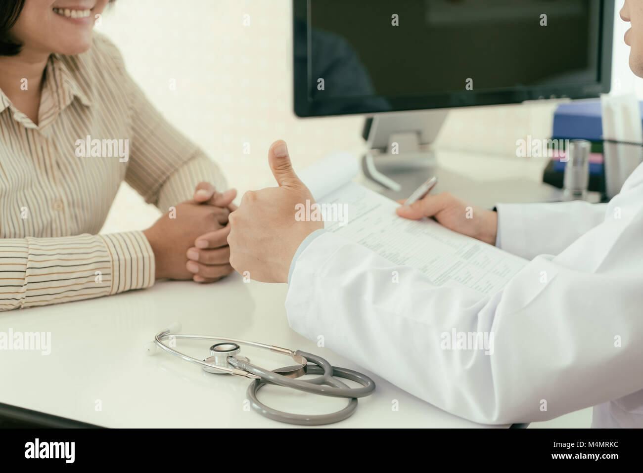 Arzt zeigen Daumen bis zu Frau Patienten für gute Nachrichten. Frau geduldig lächelnd beim Hören gute Nachrichten berichten. Stockfoto