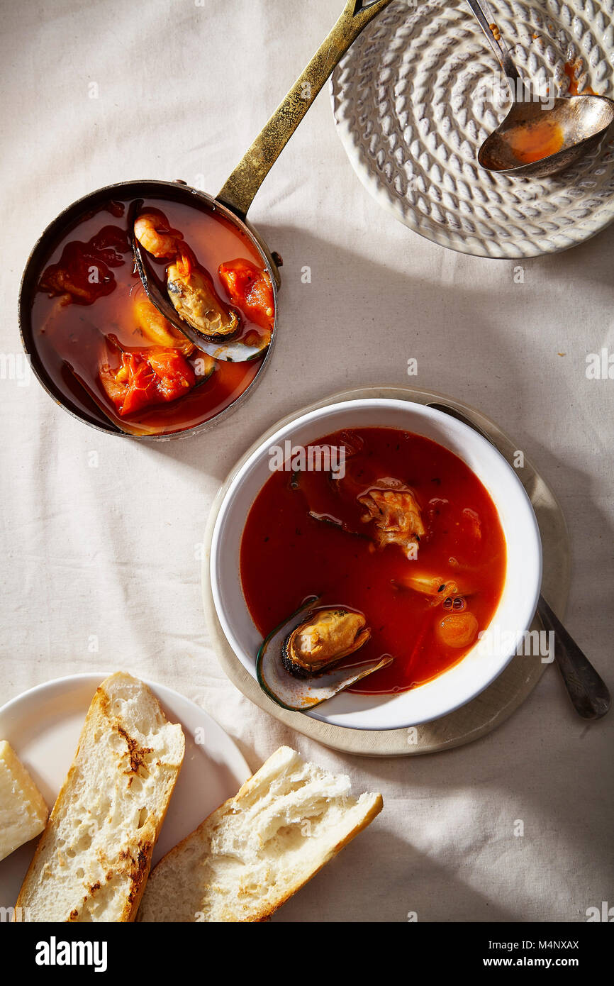 Traditionelle mediterrane Fischsuppe bouillabaisse mit Muscheln, Garnelen, Tomaten und Brühe in Kupfer Topf, und weiße Schüssel mit warmen Baguett serviert. Stockfoto