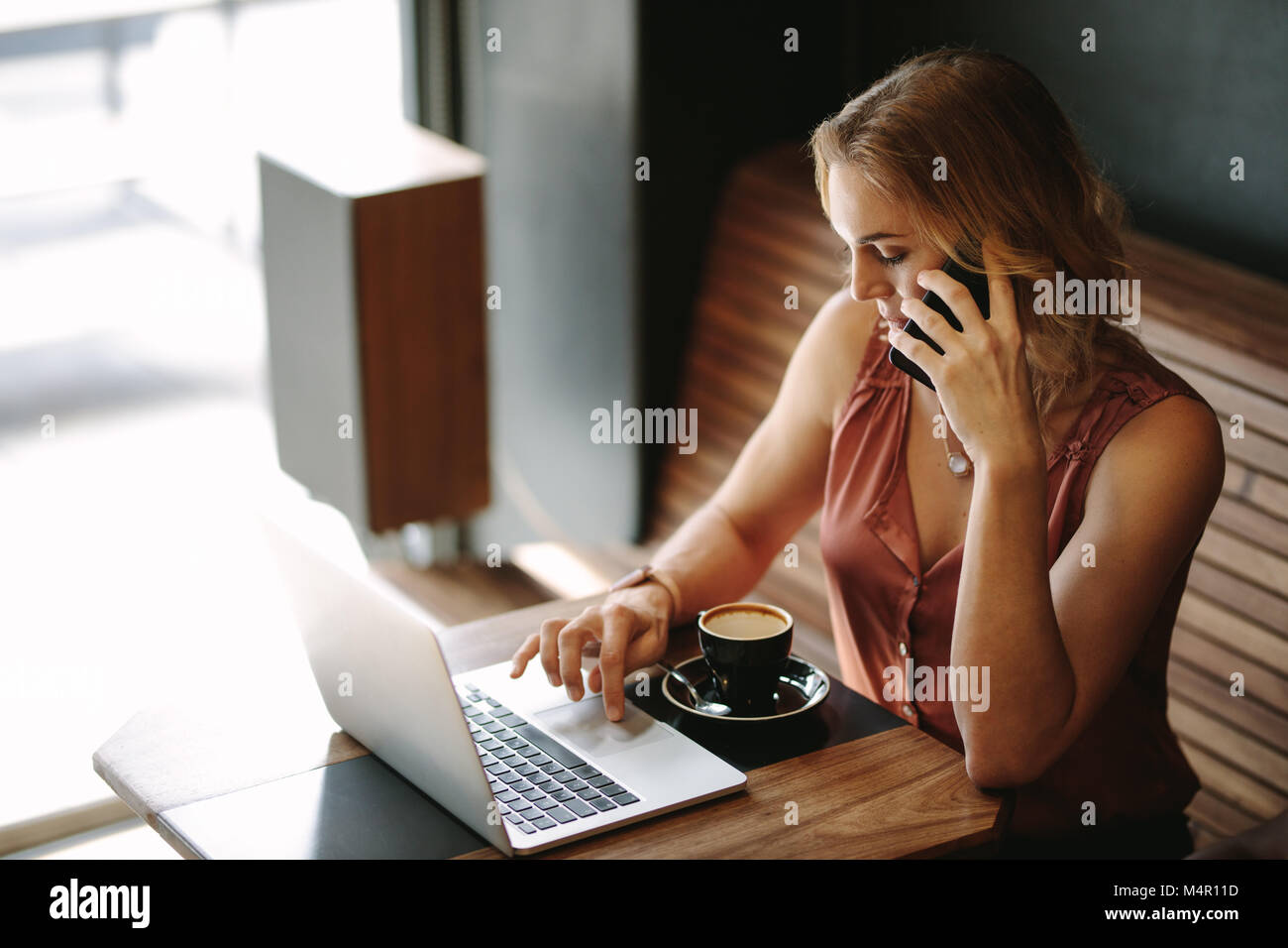 Freelancer an einem Tisch sitzen, Arbeiten am Laptop während des Sprechens über Handy. Frau tun ihre Arbeit sitzen in einem Café bei einer Tasse co Stockfoto
