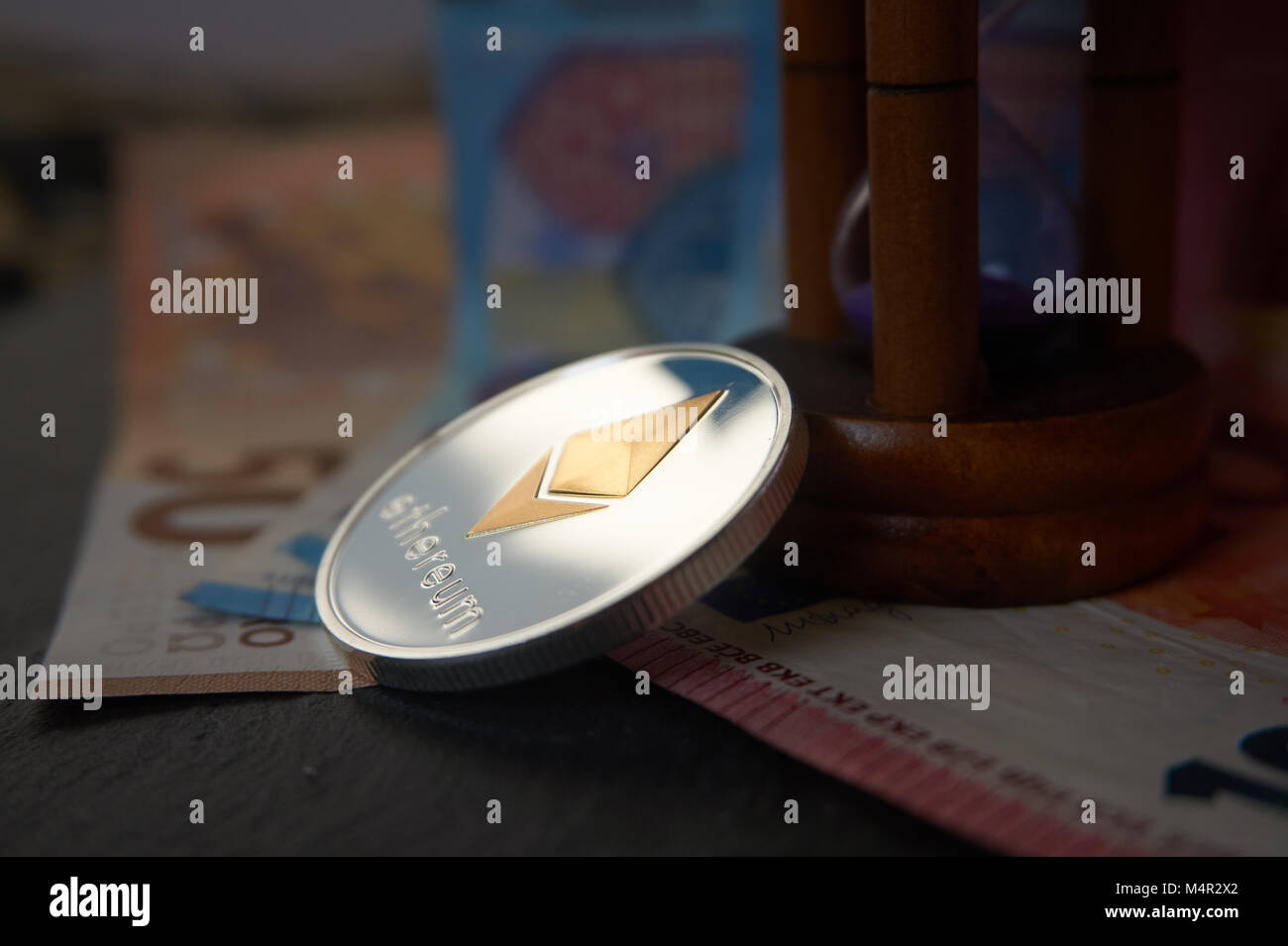 Silber Astraleums Münze und Sanduhr liegen auf der Euro-banknoten, grauen Stein Hintergrund. Cryptocurrency graben Speed Concept, selektive konzentrieren. Stockfoto