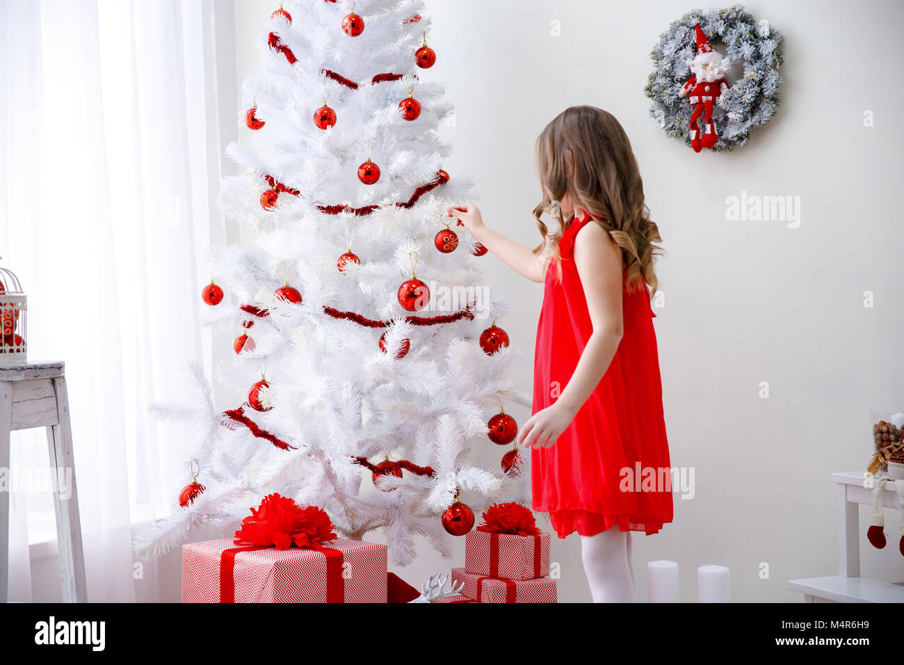 Adorable kleine Mädchen mit lockigem Haar ziert ein wunderschöner weißer Weihnachtsbaum Stockfoto