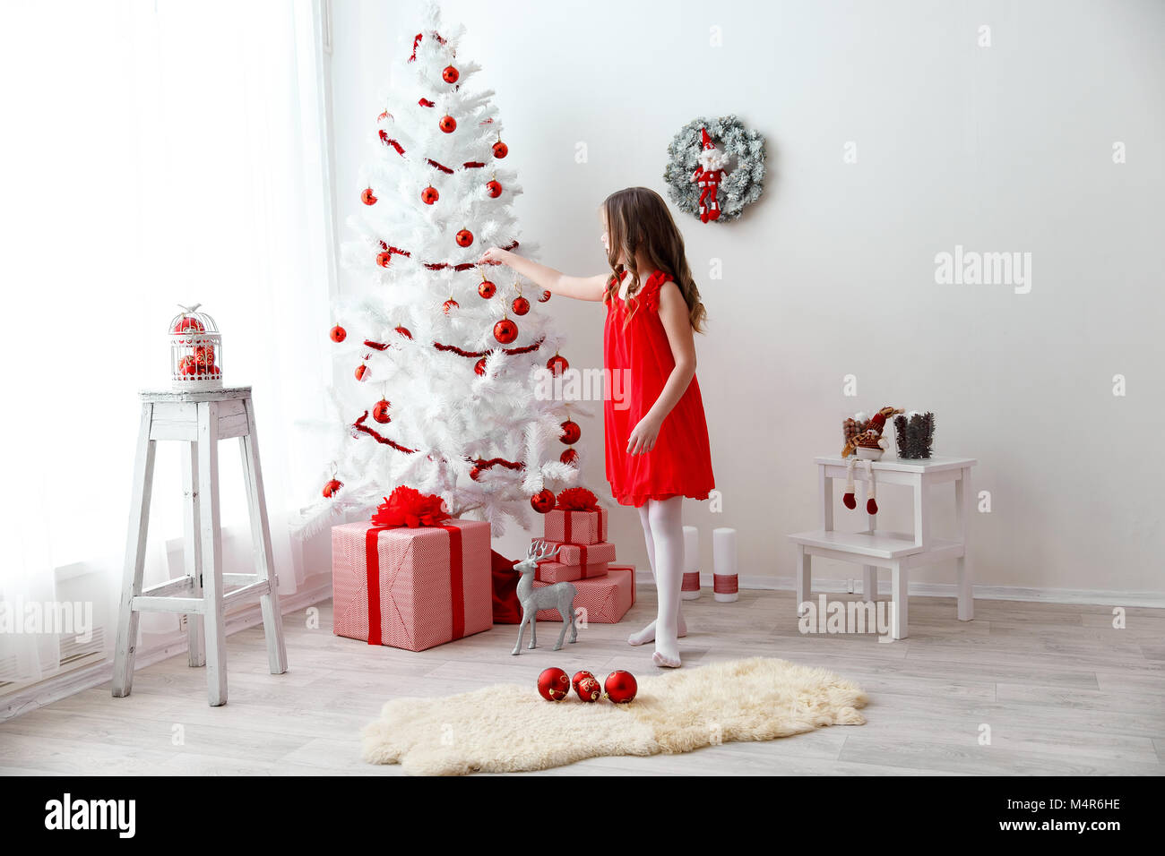 Adorable kleine Mädchen mit lockigem Haar ziert ein wunderschöner weißer Weihnachtsbaum Stockfoto