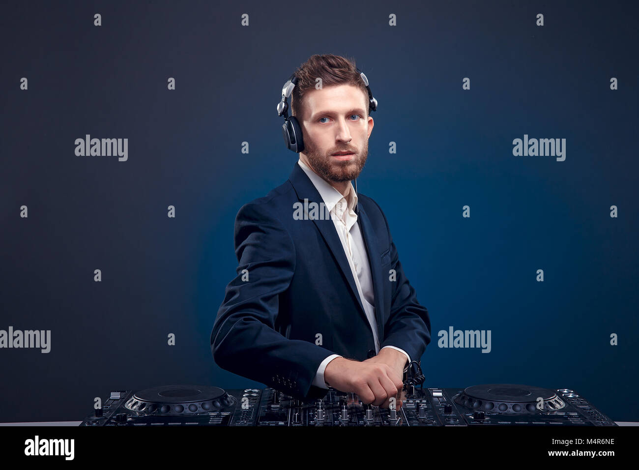 Closeup Portrait von DJ überzeugt mit eleganten Frisur und Kopfhörer am Hals mischen Musik mixer beim Stehen auf dunklem Blau, Cyan Hintergrund isoliert Stockfoto