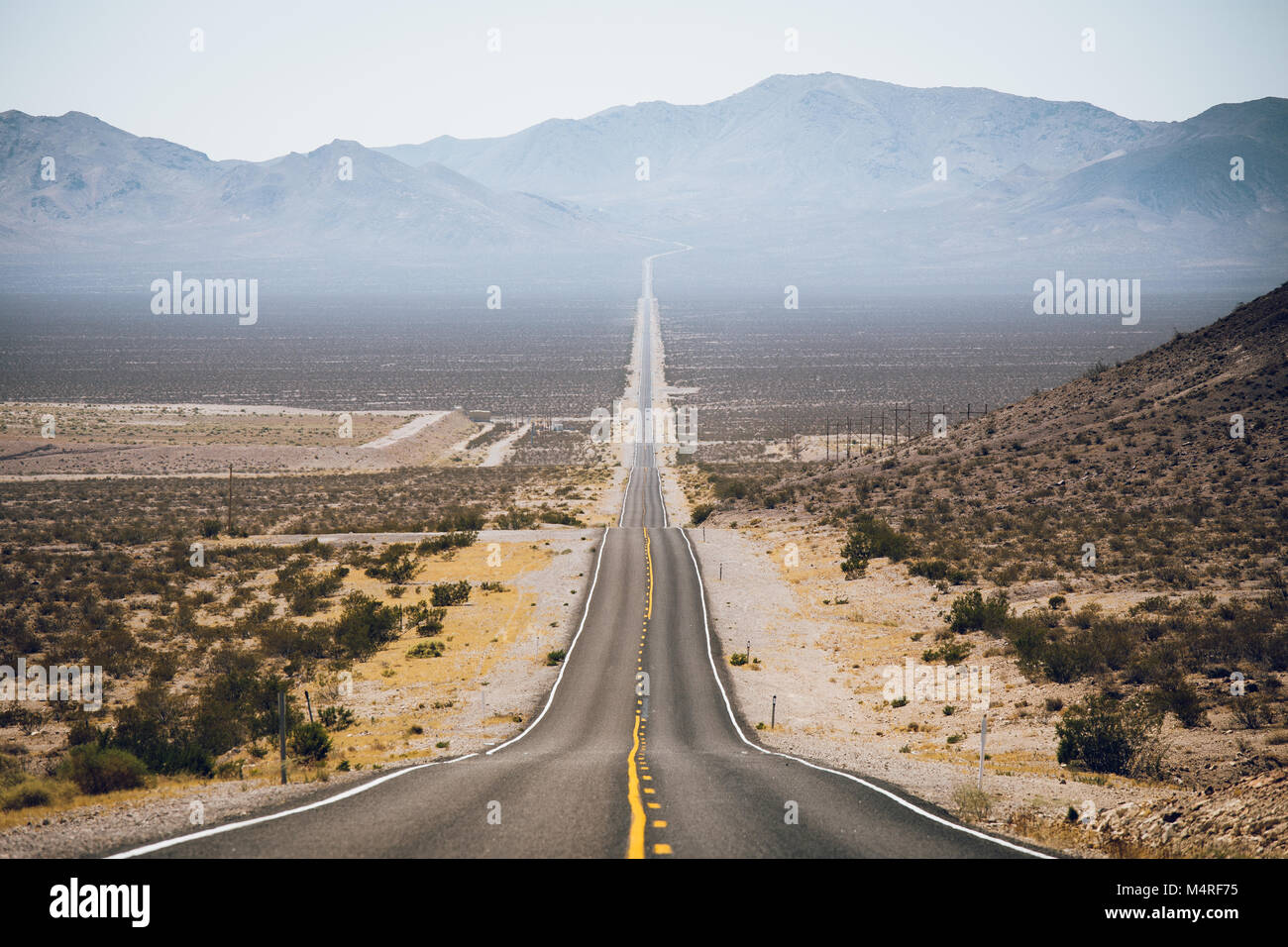 Klassische Ansicht eines endlosen geraden Straße durch die karge Landschaft des amerikanischen Südwestens läuft Stockfoto
