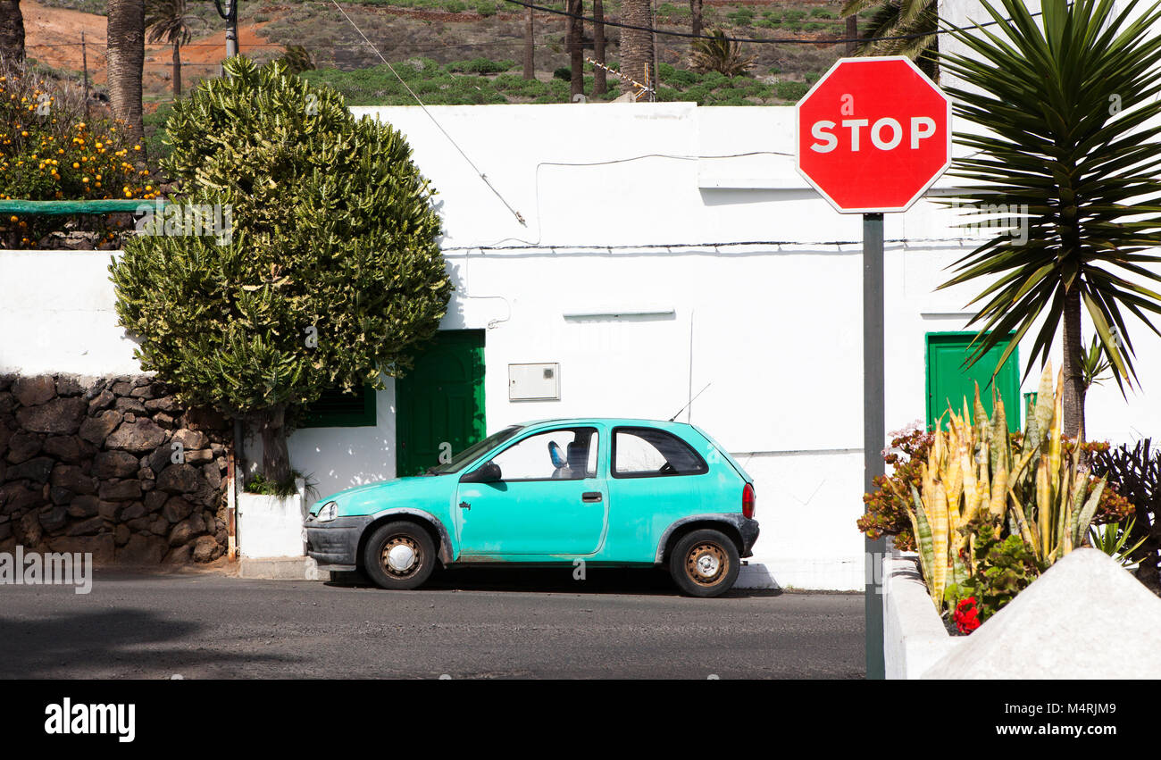 Farben von Lanzarote, ein helles farbiges Auto vor ein Typisches weißes Haus mit grünen Türen geparkt mit einem Stoppschild im Dorf Haría, Lanzarot Stockfoto