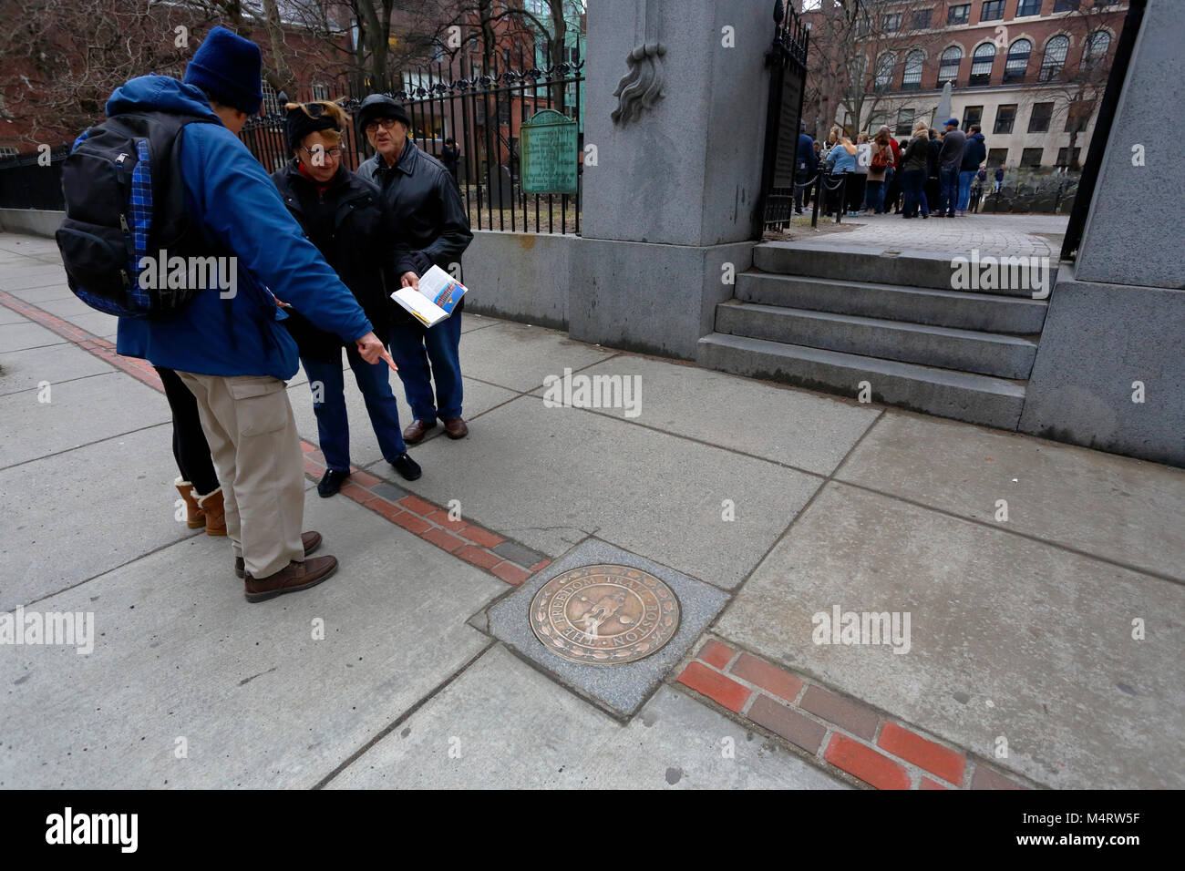 Touristen, die auf eine bronzene Gedenktafel für den Freedom Trail verweisen, die den Ort eines berühmten Wahrzeichen markiert, den Granary Burying Ground, Boston, Massachusetts Stockfoto