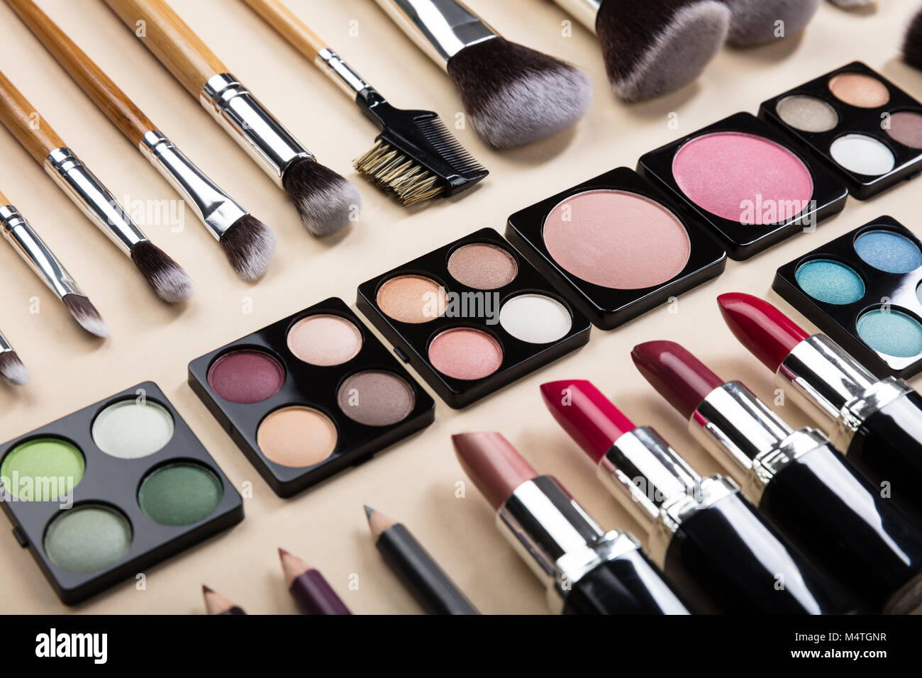 Verschiedene Arten von Make-up-Pinsel und Make-up-Produkte in einer Reihe auf beigem Hintergrund angeordnet Stockfoto