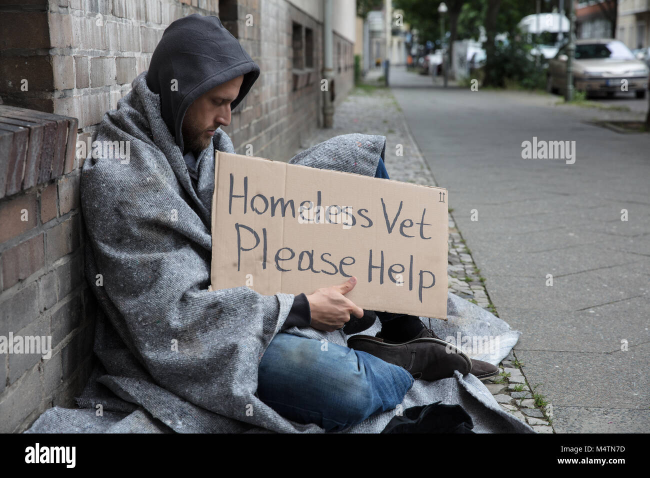 Männliche Obdachlose Sitzen auf einer Straße mit Zeichen um Hilfe zu bitten, in der Stadt Stockfoto