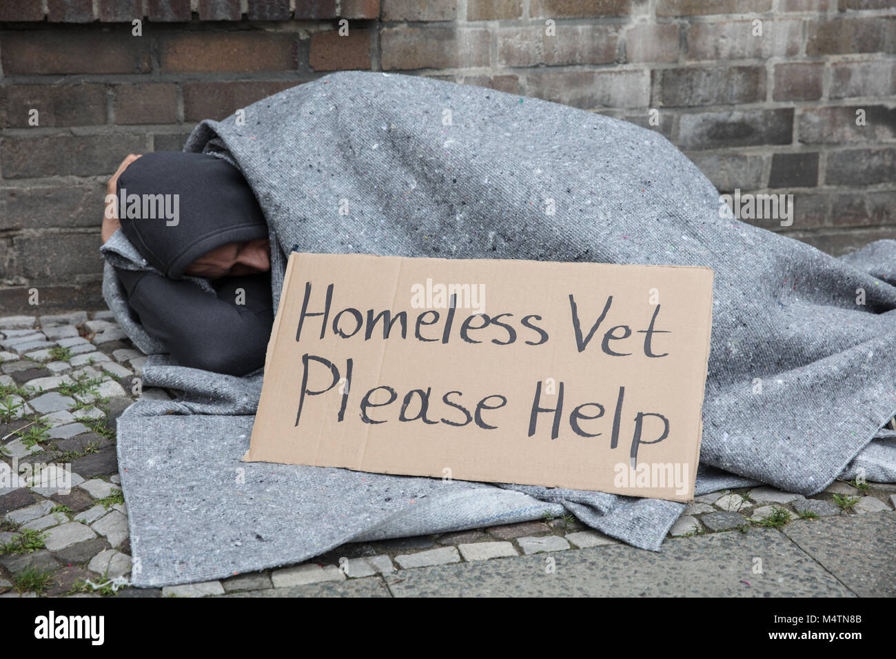 Männliche Obdachlose Sitzen auf einer Straße mit Zeichen um Hilfe zu bitten, in der Stadt Stockfoto