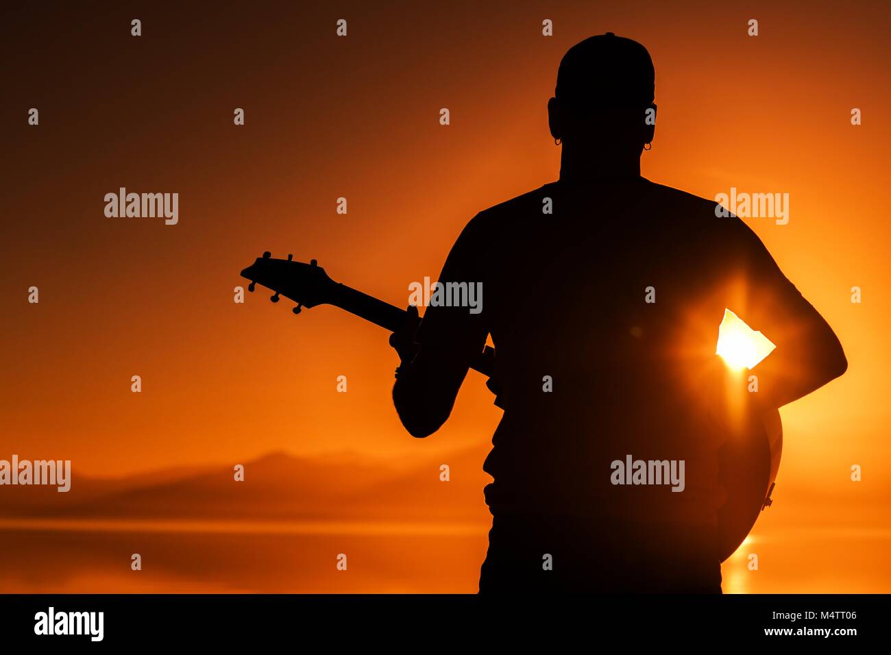 Gitarre spielen bei Sonnenuntergang. Männer mit akustischer Gitarre während des malerischen Sonnenuntergang. String Instrument Thema Stockfoto