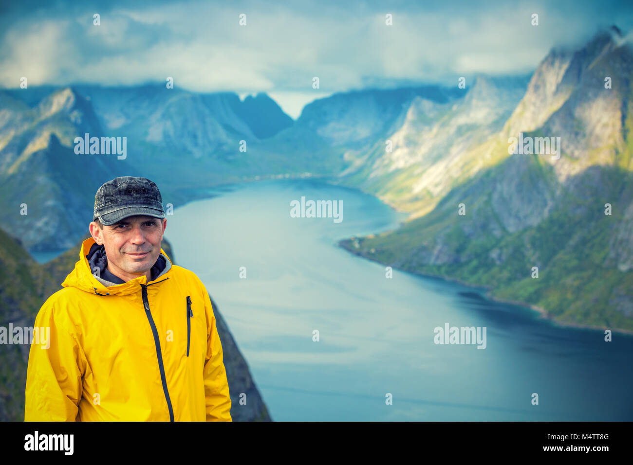 Porträt eines touristischen Mann, stehen auf einem Gipfel eines Berges Reinebringen und Suchen in der Kamera. Schöne Berglandschaft im Hintergrund. Art der Stockfoto