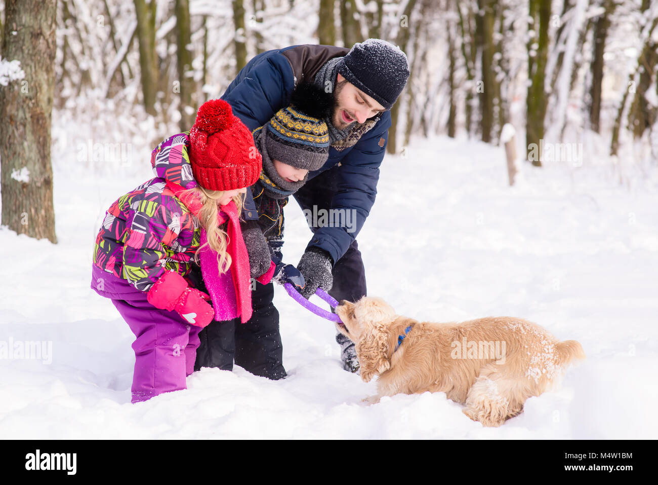 Happy Family spielen mit einem Hund im Schnee im Freien Stockfoto