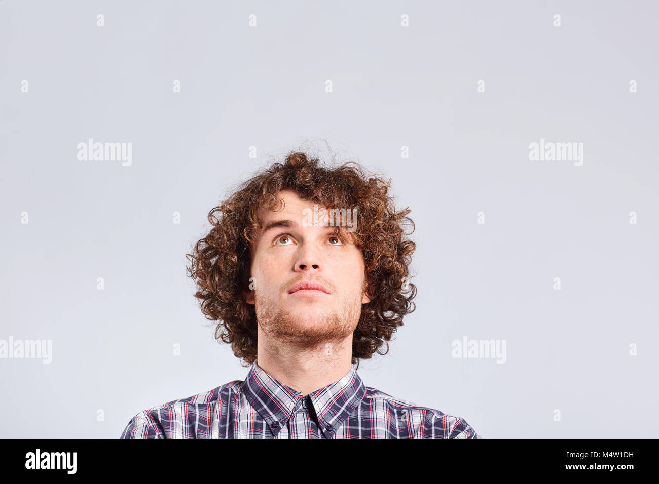 Ein curly-haired Kerl denkt mit einer ernsten Emotion. Stockfoto