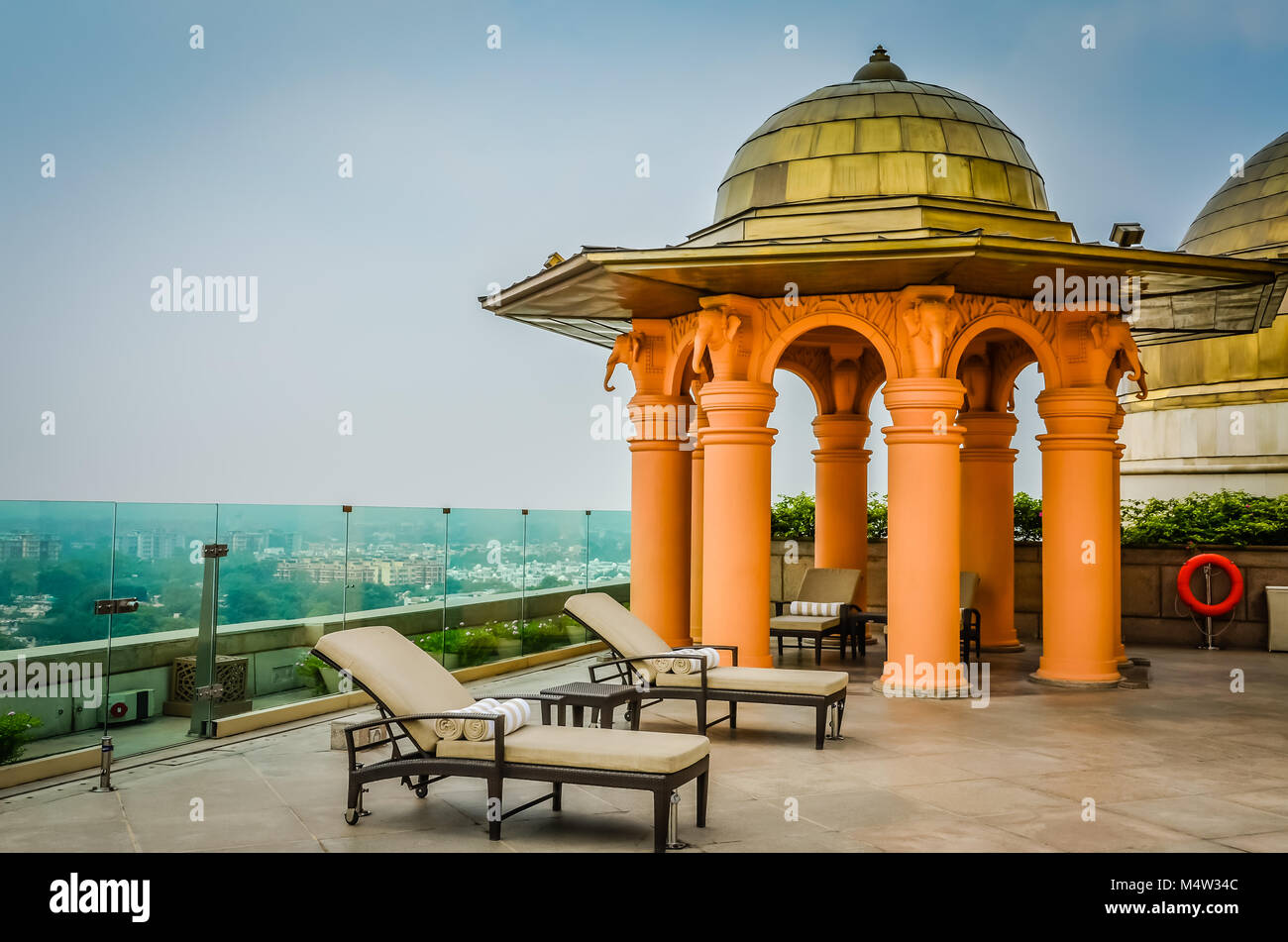 Leere Dachterrasse mit Blick in New Delhi, Indien. Glas fechten umgibt, Liegestühle mit gestreiften Tan und weiße Handtücher prepped Neben einem gold Dom Stockfoto
