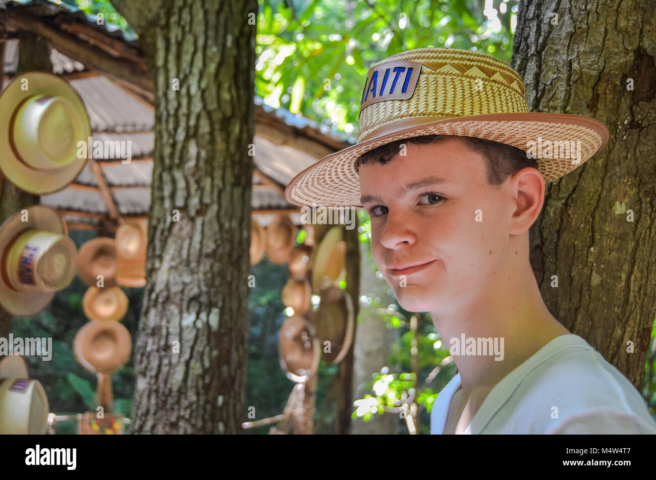 Labadee, Haiti. Porträt einer teenaged Jungen tragen ein handcrafted straw hat vor dem Hintergrund der Bäume und der Markt. Stockfoto
