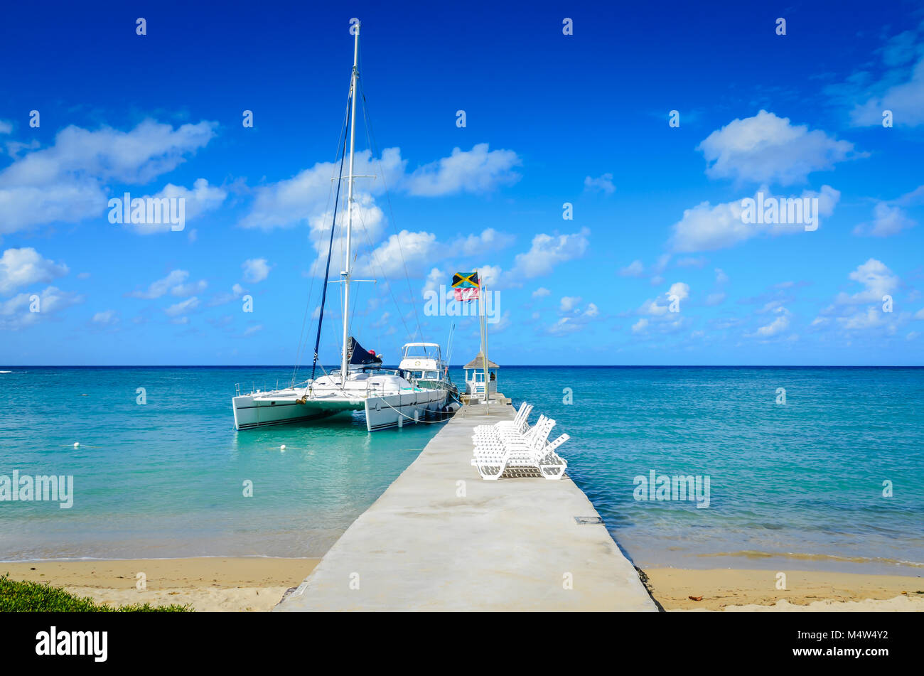 Jamaika. Konkrete Dock mit Pavillon und Liegestühlen, Segelboot angedockt an der Seite. Stockfoto