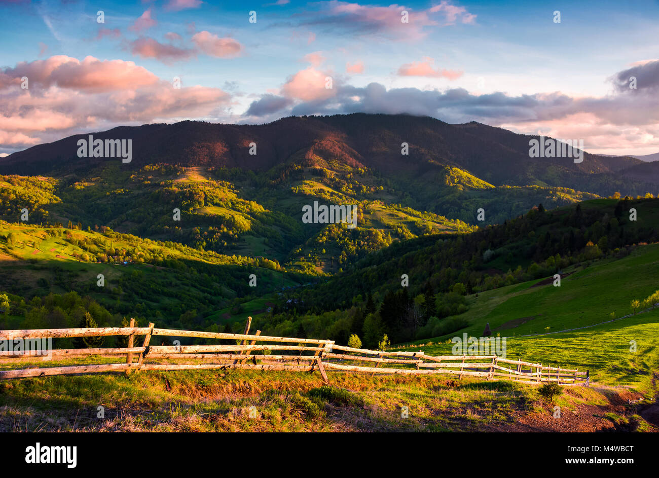 Wunderschönen Abend im bergigen Land. Zaun entlang der grasigen Hang. bergrücken unter der violetten Wolken an einem blauen Himmel. schöne Landschaft im fi Stockfoto