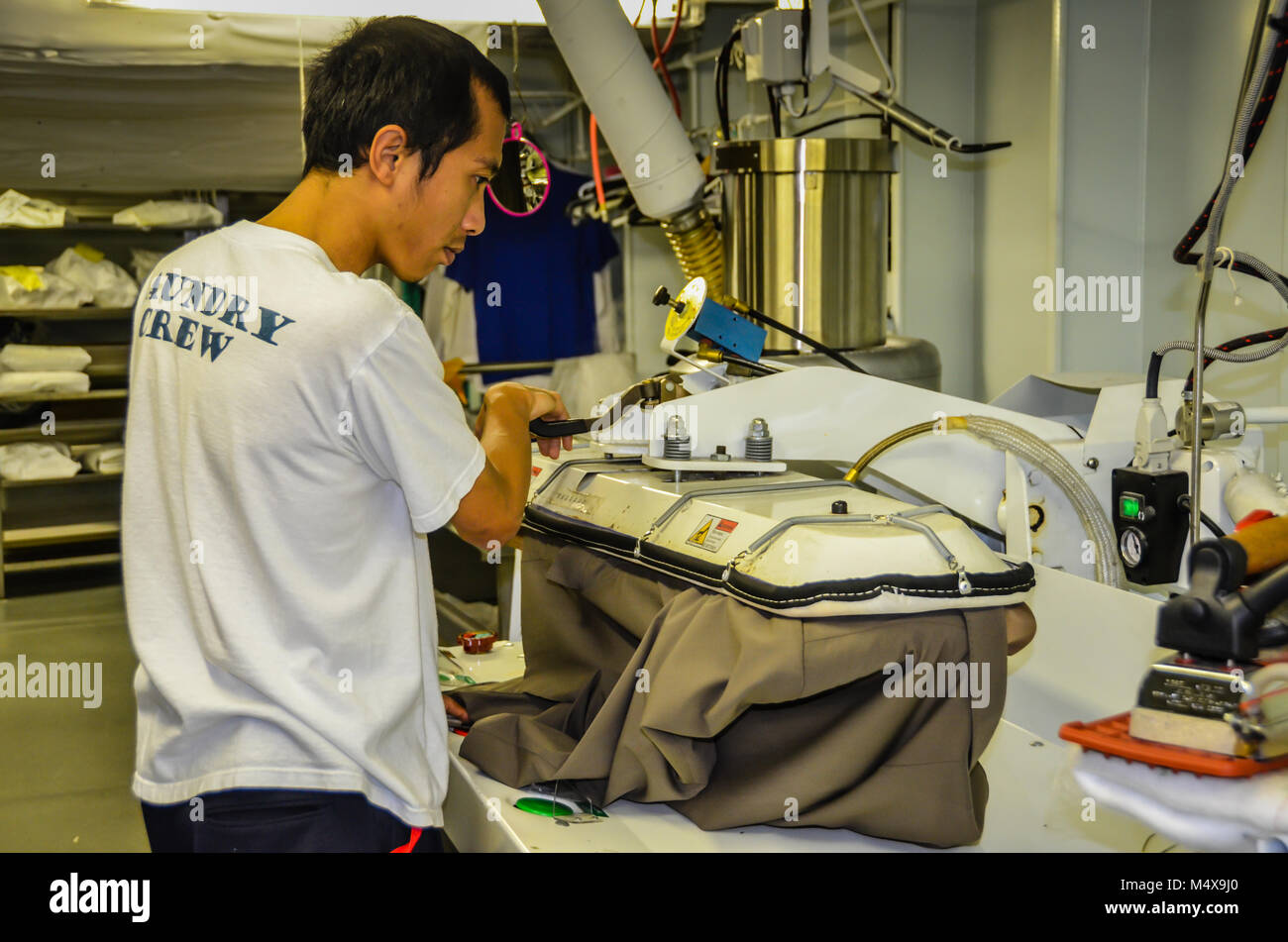 Wäscheservice Arbeiter pressen Anzugjacke auf industriellen Eisen in großer Waschraum Ausstattung des Kreuzfahrtschiffes. Stockfoto