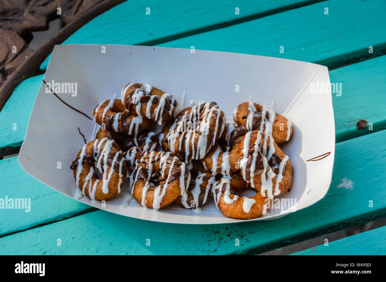 Faltschachtel mit Mini Donuts verglast mit weißem Zucker und Schokolade Sahnehäubchen auf Green Table Top Hintergrund platziert. Stockfoto