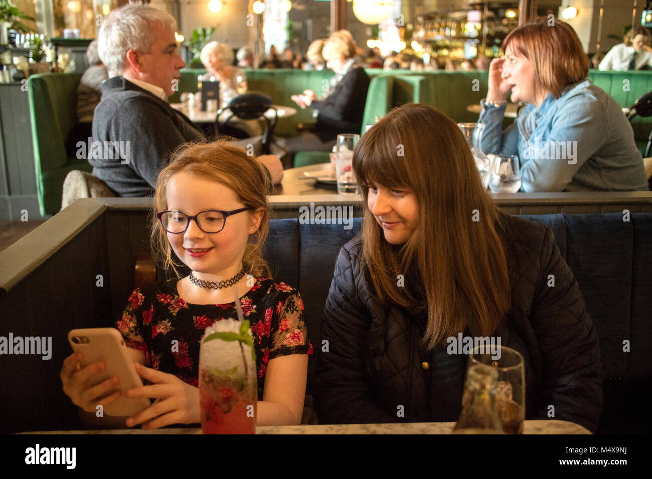 Mutter und 8 Jahre alten Tochter in einer belebten Bar suchen und Spielen auf dem Apple iPhone Stockfoto