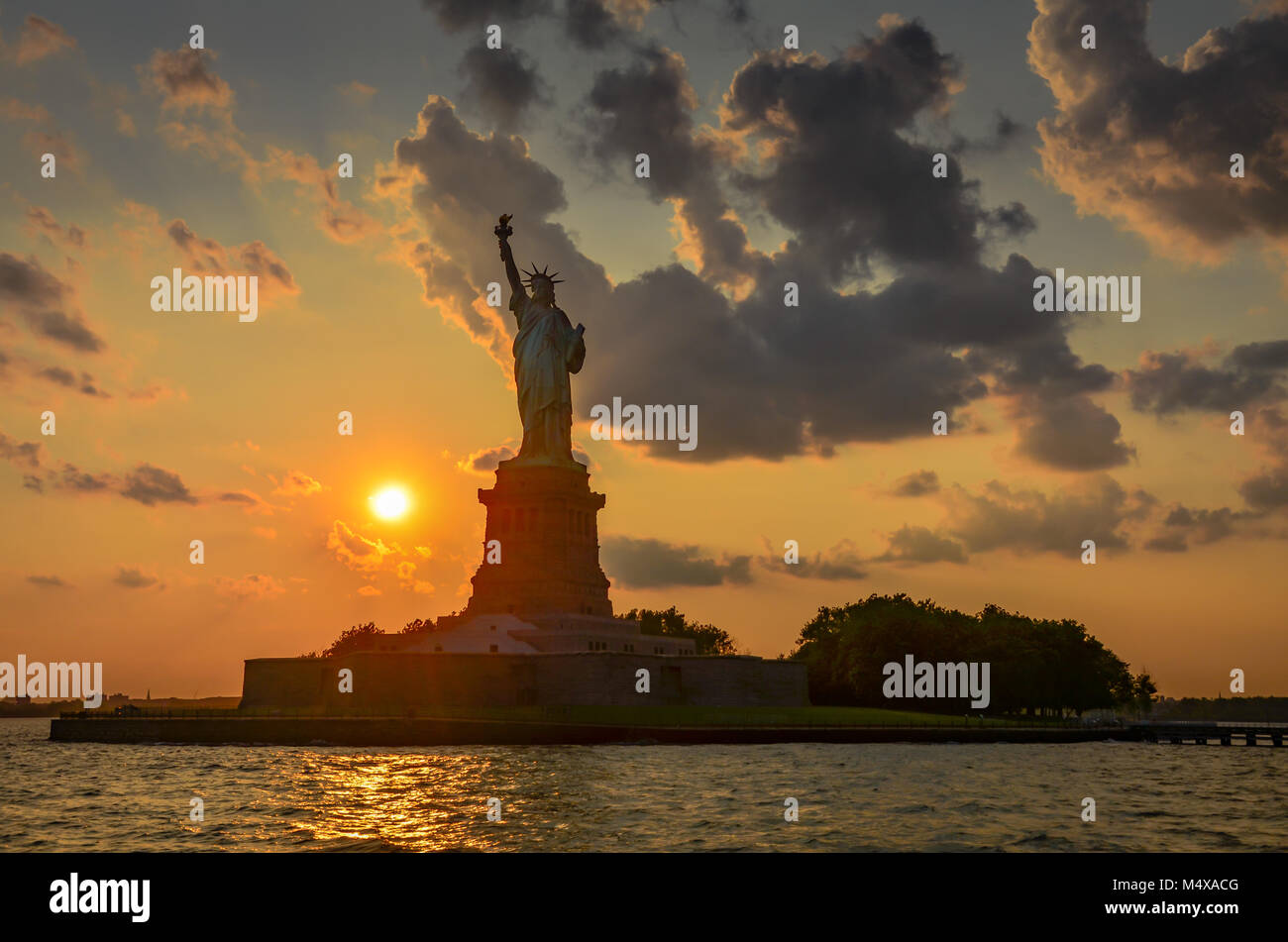 Untergehenden Sonne malt eine lebendige und bunte Himmel hinter der Freiheitsstatue in New York City. Stockfoto